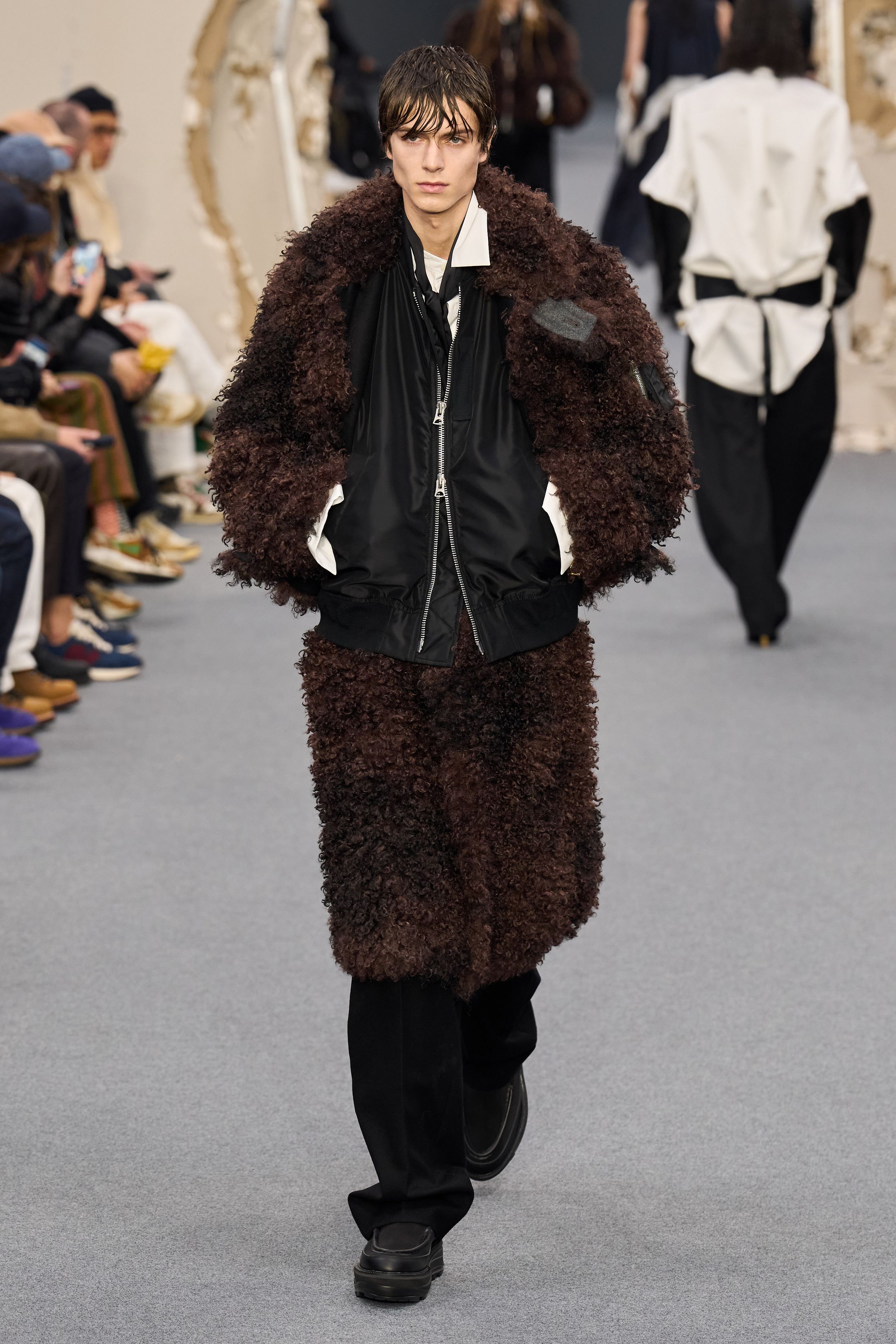 Sacai 2026秋冬再次展示其无可复制的“混合美学”。正装、牛仔、皮草与制服元素被高度结构化地拼接，形成既熟悉又陌生的服装形态。性别边界被进一步模糊，层叠结构制造流动节奏，使行走本身成为设计的一部分。系列在秩序与混乱之间找到平衡，是Sacai 对当代复杂生活状态的持续回应-顽石频道趋势研究